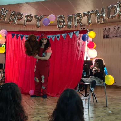 אישה עם בובה על במה עם בלונים וקישוטי יום הולדת