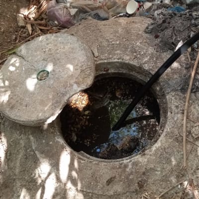 צינור שחור בתוך פתח ביוב עם מכסה בטון