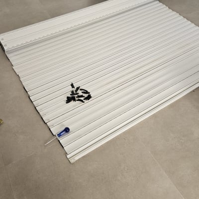 תריסים לבנים מונחים על הרצפה עם מברג