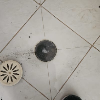 רצפת קרמיקה עם פתח ניקוז עגול ופסולת סביבו