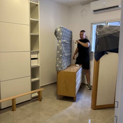 אדם מזיז מזרן עטוף בחדר ריק עם רהיטים