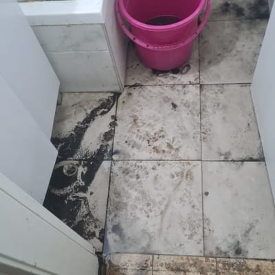 רצפה מלוכלכת עם דלי ורגליים של אינסטלטור