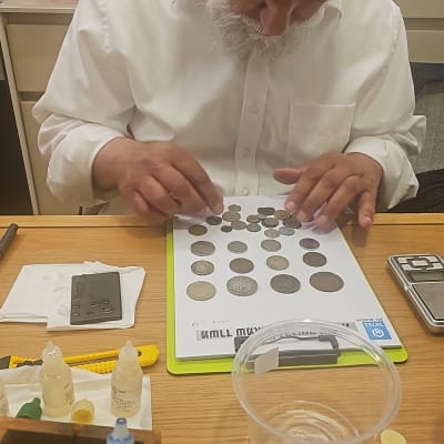 אדם בוחן מטבעות על שולחן עם כלים שונים