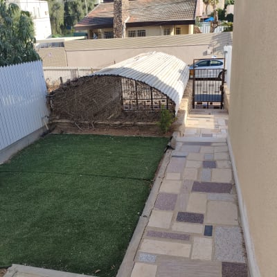 שביל מרוצף לצד דשא סינתטי וגדר עץ לבנה