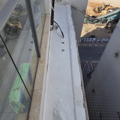 עבודת איטום בחומר לבן על גבי אדנית חיצונית במרפסת בגובה