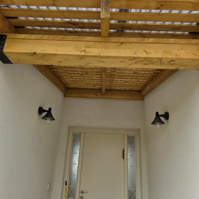 פרגולה מעץ מעל כניסה לבית עם דלת לבנה