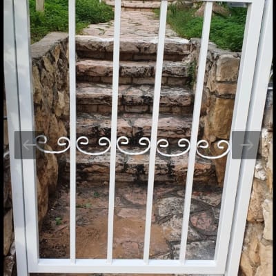 שער מתכת לבן עם עיטורים, מדרגות אבן מאחוריו