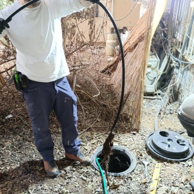 אדם מחזיק צינור ליד פתח ביוב פתוח