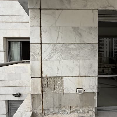 קיר חיצוני עם אריחים שבורים ותיקונים נראים לעין