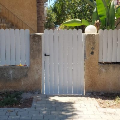 שער עץ לבן עם ידית שחורה על גדר בטון