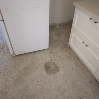 רצפה מלוכלכת עם כתמים ליד מקרר וארון מטבח