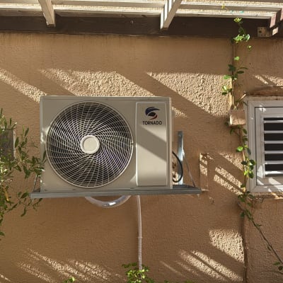 יחידת מיזוג אוויר מותקנת על קיר חיצוני עם צמחייה מסביב