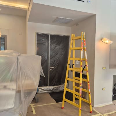 סולם צהוב בחדר עם קירות צבועים וציוד מכוסה בניילון