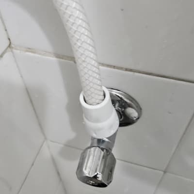ברז ניל זוויתי מחובר לצינור מים גמיש על קיר אריחים לבן
