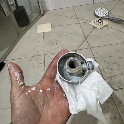 יד מחזיקה חלק מתכת עם חור, רקע מקלחת