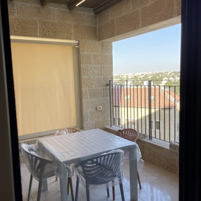 מרפסת עם שולחן וכיסאות פלסטיק, גג עץ ותצפית לנוף עירוני