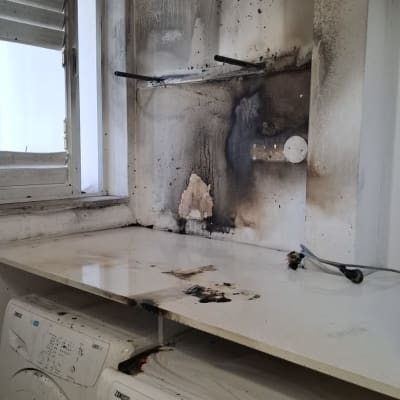 קיר עם כתמי פיח ושריפה ליד מכונת כביסה