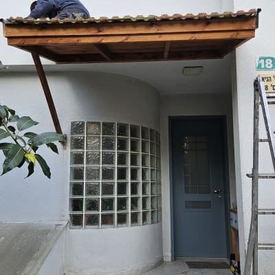 אדם עובד על גג עץ קטן מעל כניסה לבית