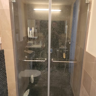 מקלחון עם דלתות זכוכית, בקבוקי שמפו ומקלחת יד