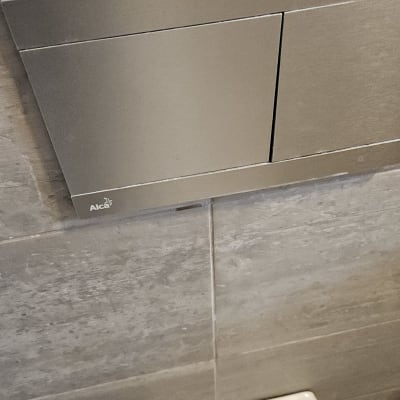 לחצן הדחה לאסלה על קיר אריחים אפור