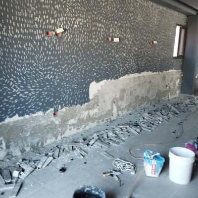 קיר צבוע חלקית עם דוגמאות צבע, דלי צבע וכלים על הרצפה