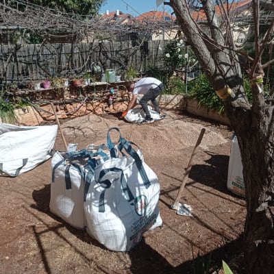 אדם עובד בגינה עם שקי אדמה וכלי גינון