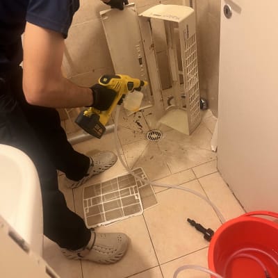 אדם מנקה חלקי מזגן בחדר אמבטיה עם כלי עבודה