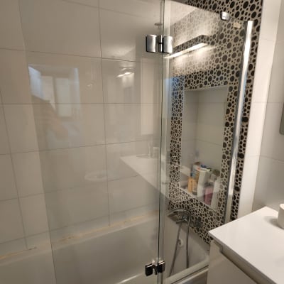 מקלחון עם דלת זכוכית ומדף מוצרי טיפוח