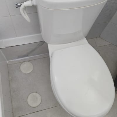 אסלה לבנה עם חיבורי צנרת על רצפת אריחים