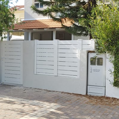 גדר עץ לבנה ליד עץ ושיח ירוק