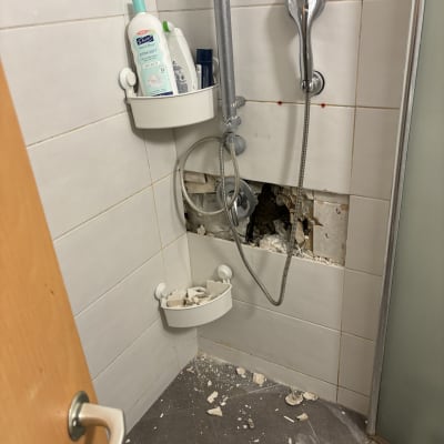 חלק מקיר מקולף במקלחת עם צינור מים חשוף