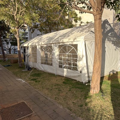 אוהל לבן גדול מוצב על דשא ליד עצים