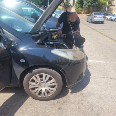 אדם בודק מנוע של רכב עם מכסה פתוח