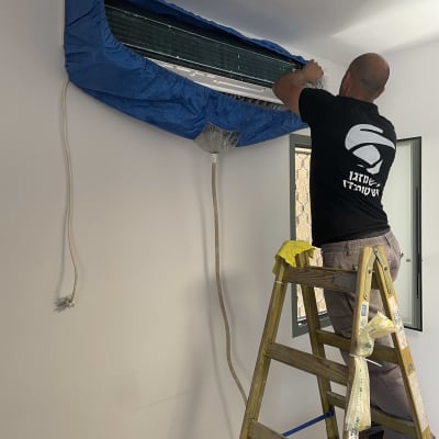 טכנאי מתקין כיסוי כחול על מזגן קיר