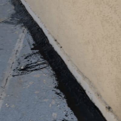 יישום חומר איטום ביטומני שחור בחיבור בין הגג לקיר