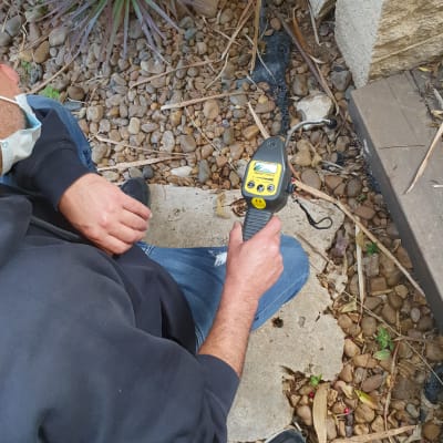 אדם מחזיק מכשיר איתור צינורות על קרקע עם אבנים