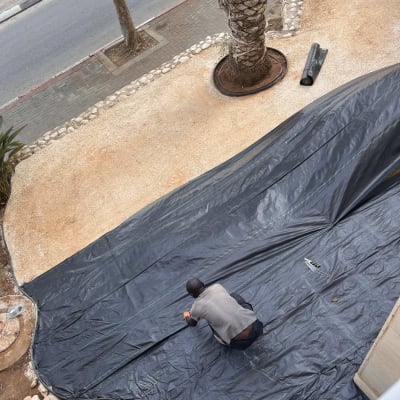 אדם פורש יריעת פלסטיק שחורה בגינה