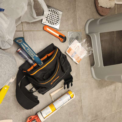 כלי עבודה של אינסטלטור על רצפה, כולל מפתח צינורות, סכין יפנית, אקדח סיליקון.