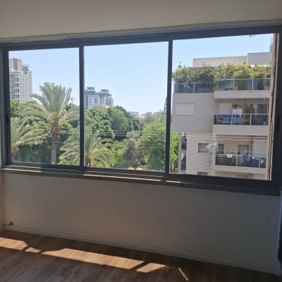 חלון אלומיניום עם נוף לעיר ועצים ירוקים