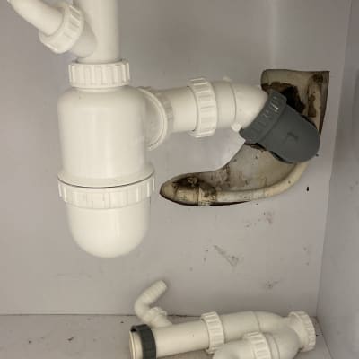 צינורות פלסטיק לבנים מתחת לכיור עם חיבורים אפורים