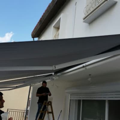 שני אנשים מתקינים סוכך אפור על קיר חיצוני