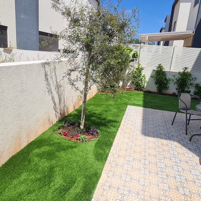 עץ קטן על דשא מלאכותי עם פרחים מסביב