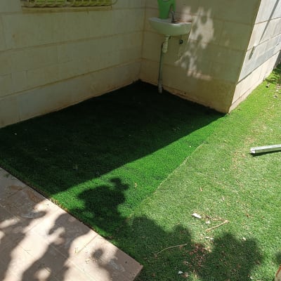 דשא סינתטי מותקן ליד קיר עם כיור חיצוני