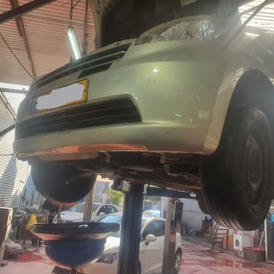 רכב מורם על ליפט במוסך עם כלי איסוף שמן