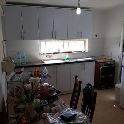 מטבח עם ארונות לבנים, כיור וברז, בקבוקי מים