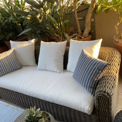 כריות לבנות וכחולות על ספה קלועה בגינה