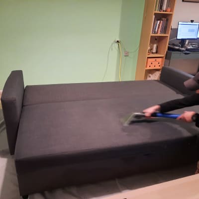 אדם מנקה ספה עם מכשיר ניקוי ידני