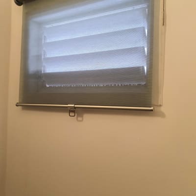 תריסים עם וילון גלילה אפור על חלון קטן