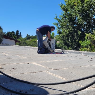 אדם עובד על מזגן על גג תחת שמיים כחולים