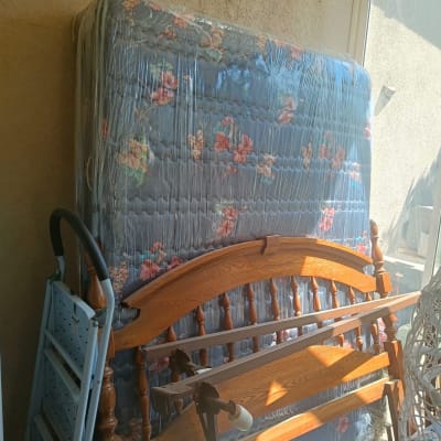 מזרן וראש מיטה מעץ מונחים בצד חדר מואר.